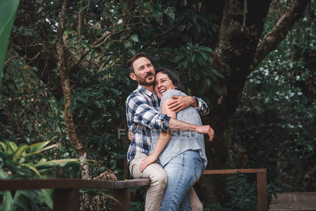 Веселая влюбленная пара обнимается на деревянной террасе дома в лесу и смеется — стоковое фото