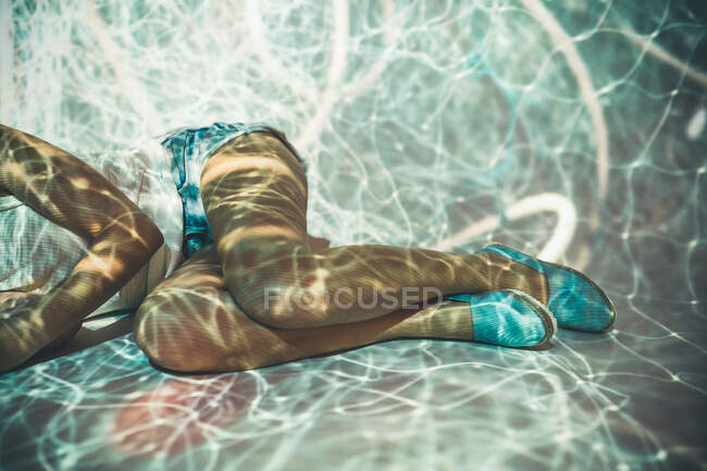 Colheita jovem fêmea em roupas casuais deitado em projeção de luz abstrata de linhas brancas emaranhadas — Fotografia de Stock