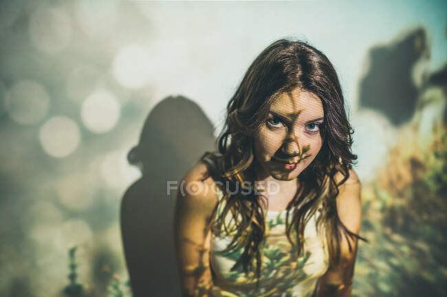 Высокий угол взгляда молодой женщины на камеру, стоящей напротив стены с травянистой проекцией поля — стоковое фото