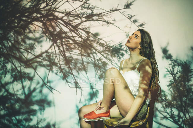 Молода жінка сидить на стільці і дивиться на проекцію листяних гілок дерева — стокове фото