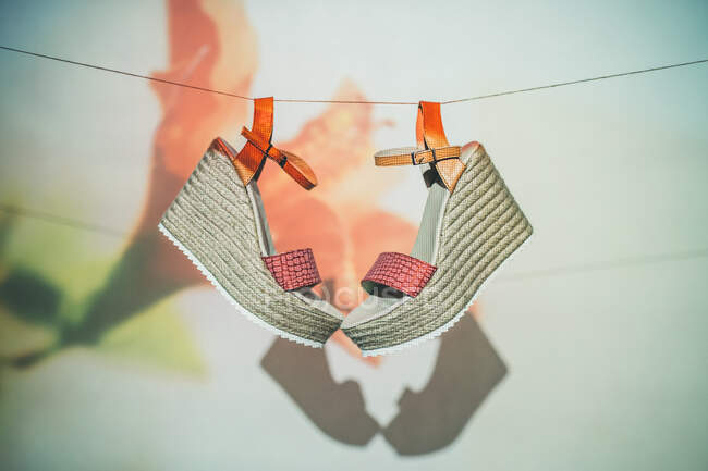 Trendy sandals hanging on rope against wall with projection of flower in summer — Stock Photo