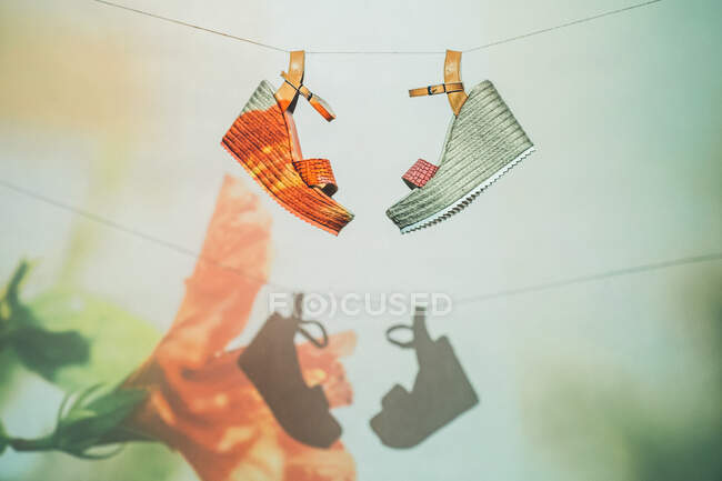 Sandálias da moda penduradas na corda contra a parede com projeção de flor no verão — Fotografia de Stock