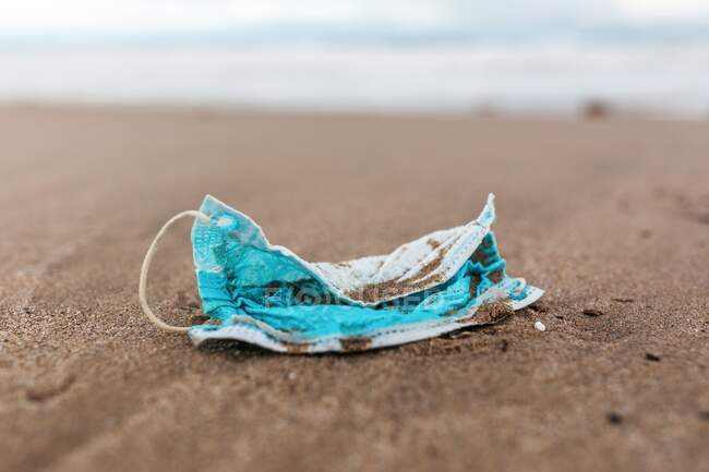 Máscara protetora usada na praia lavada por ondas marítimas mostrando conceito de poluição ambiental com resíduos médicos — Fotografia de Stock