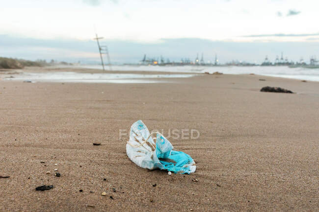 Брудні медичні маски на піщаному пляжі, що показують концепцію забруднення пластиковими відходами — стокове фото