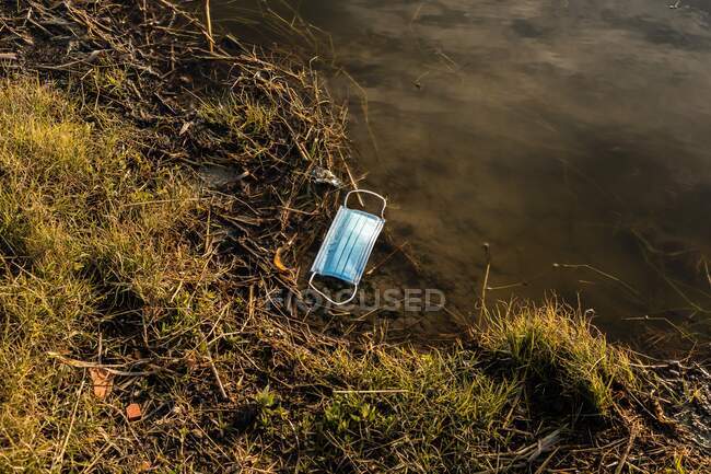 Von oben eine medizinische Maske aus Plastik, die auf dem Teichwasser schwimmt und das Konzept der Umweltverschmutzung mit Plastik zeigt — Stockfoto