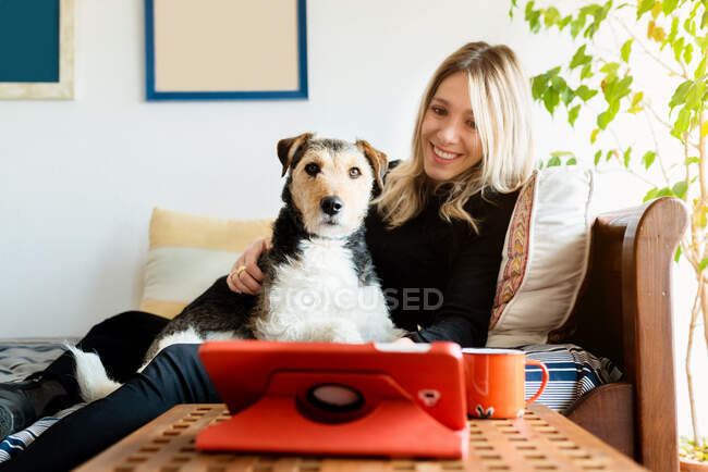 Amigável fêmea interagindo com cão de raça pura atencioso contra tablet com tela preta na mesa em casa — Fotografia de Stock