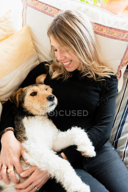 D'en haut de Candid femelle embrassant chien de race mignon tout en se reposant sur un lit doux avec des coussins à la maison — Photo de stock