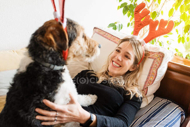 From above happy female in decorative deer horns cuddling adorable purebred dog on bed — Stock Photo