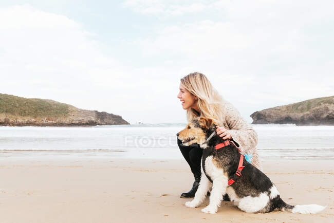 Side view of woman hugging cute purebred dog while looking away against sea under cloudy sky — Stock Photo