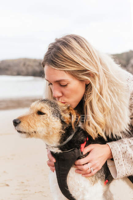 Side view of woman kissing cute purebred dog while standing against sea under cloudy sky — Stock Photo