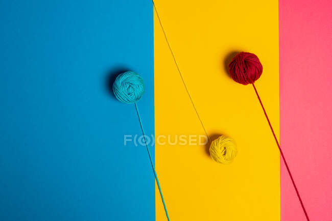 Desde arriba de pequeñas bolas de hilo de lana que representan los lollies en palos sobre fondo azul, amarillo y rosa - foto de stock
