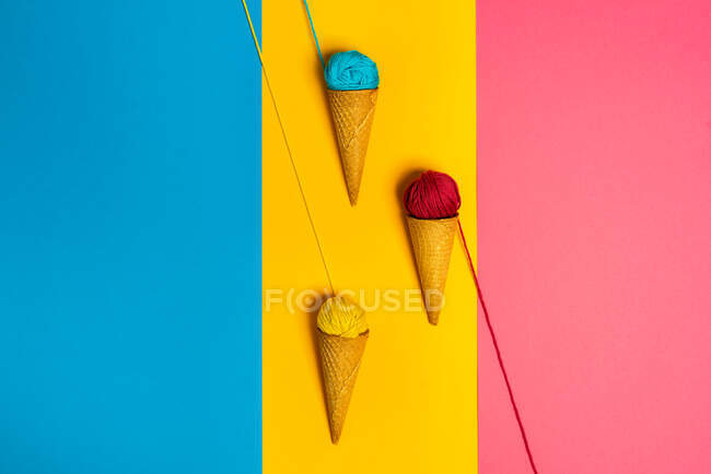 Bolas de hilo de lana de colores en conos crujientes naturales que representan varios gelato sobre fondo de tres colores - foto de stock