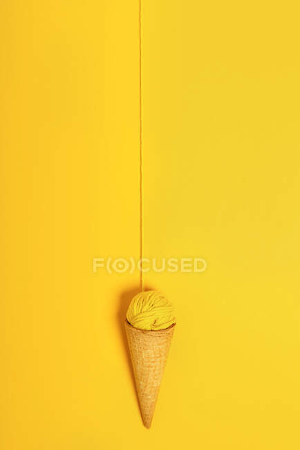 Pallina filo di lana colorato in cono croccante naturale rappresentante gelato su sfondo giallo — Foto stock