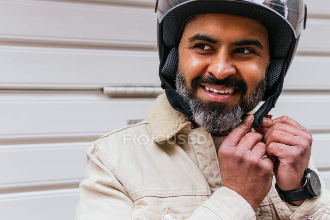 Alegre meia idade étnico masculino motociclista vestindo protetora capacete enquanto olhando para câmera contra nervuras parede — Fotografia de Stock