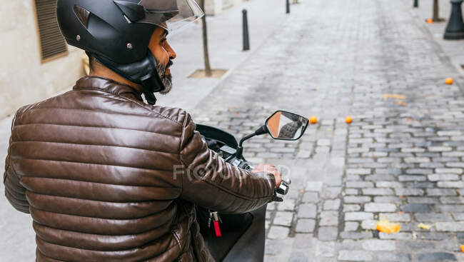 Vista trasera de brutal ciclista masculino étnico en casco de conducción de motocicletas contemporáneas mientras mira camino en la ciudad - foto de stock