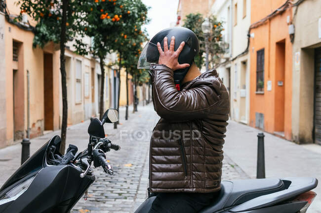 Vista lateral de un irreconocible motociclista masculino con casco en moto en la ciudad - foto de stock