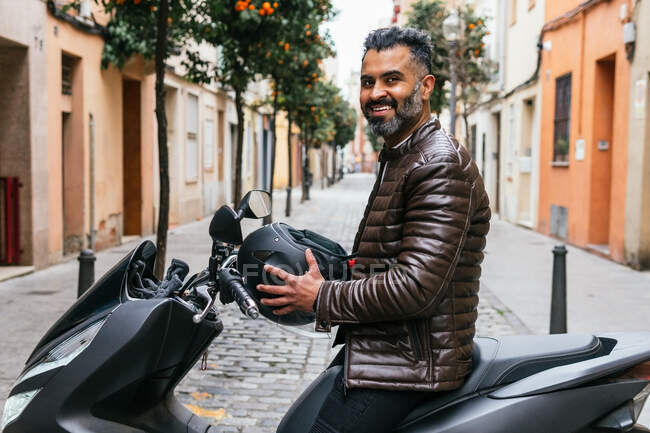 Vista lateral do conteúdo masculino motociclista hispânico masculino com capacete olhando para longe na moto na cidade — Fotografia de Stock