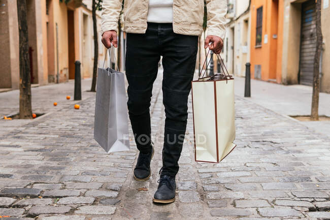 Обрезанный неузнаваемый мужчина с сумками для покупок прогуливается по городской аллее — стоковое фото