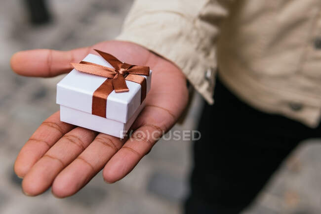 Crop anonymous male hand holding small present box with ribbon in town — Stock Photo
