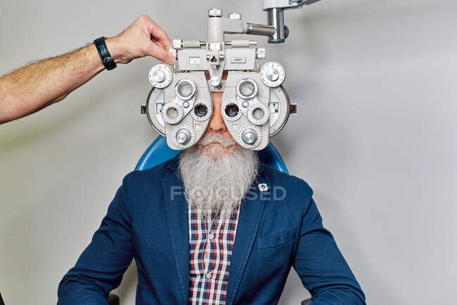 Une opticienne méconnaissable utilise un phoropter pour tester la vue d'un patient âgé de sexe masculin en clinique — Photo de stock