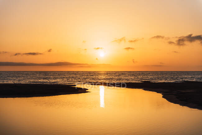 Мальовничий вид на яскраве оранжеве небо заходу сонця над спокійною морською водою ввечері — стокове фото