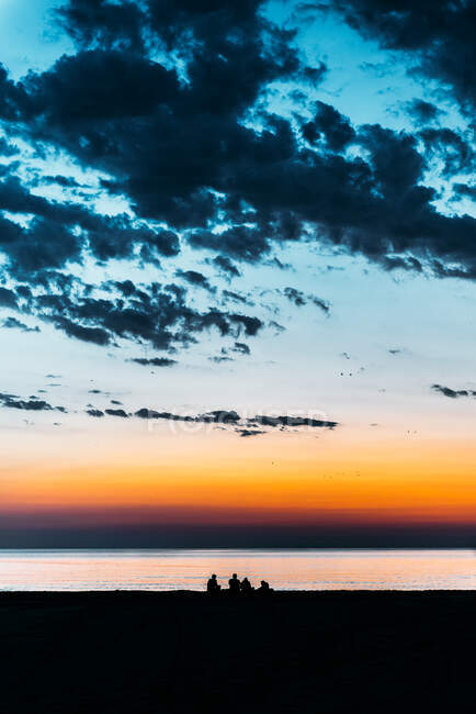 Vista posteriore di sagoma di persone irriconoscibili in piedi in acqua di mare e ammirando vista spettacolare del cielo colorato tramonto in estate — Foto stock