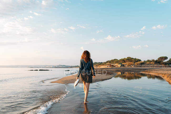 Back view of female walking in water of sea and admiring spectacular view of colorful sundown sky in summer — Stock Photo