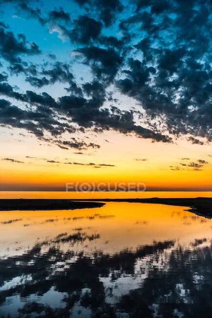 Живописный пейзаж спокойной речной воды, отражающей красочное небо с облаками на закате — стоковое фото