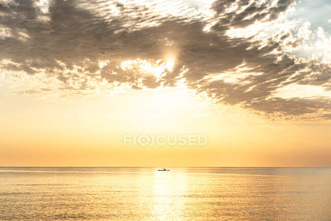 Vista remota della barca galleggiante sull'acqua increspata del mare calmo sullo sfondo del cielo luminoso tramonto — Foto stock