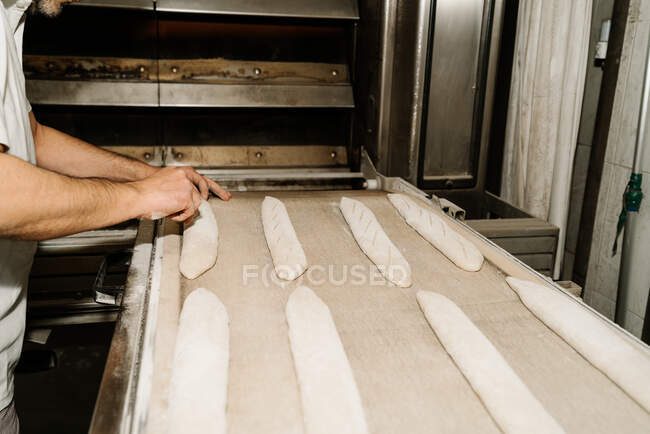 Side view of crop anonymous male baker cutting raw bread dough creating ornament on soft surface at work — Stock Photo