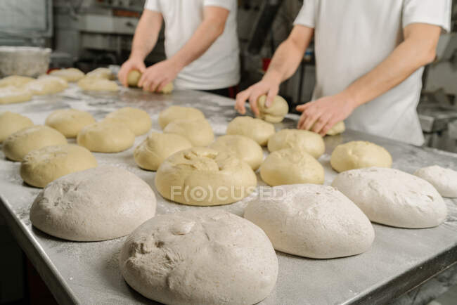 Cropped unrecognizable bakers forming bread from dough at table with flour and bowl in bakery — Stock Photo