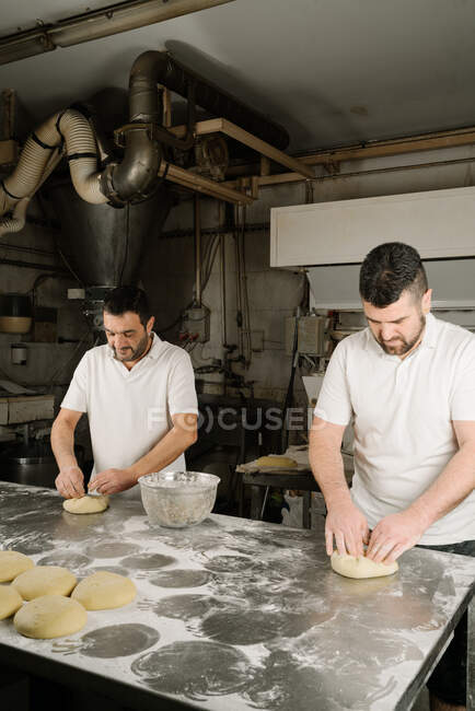 Boulangers ethniques barbus matures formant du pain à partir de la pâte à table avec de la farine et un bol dans la boulangerie — Photo de stock