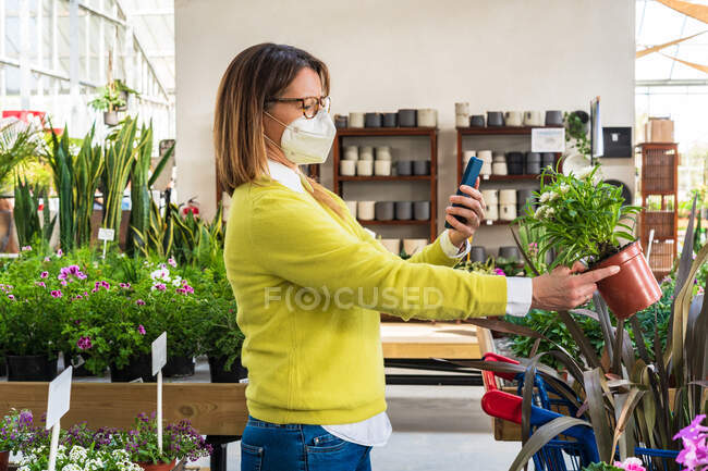 Mulher vista lateral tirar foto de flor no smartphone no centro de jardim — Fotografia de Stock