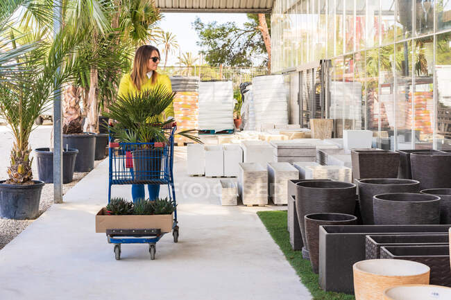 Femme client marche avec chariot dans le centre de jardin et le choix des pots pour les plantes — Photo de stock