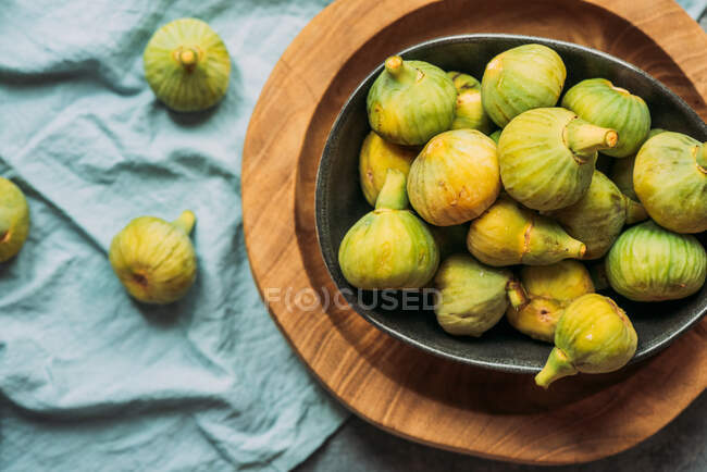 Figos verdes doces frescos e maduros, em uma tigela preta no prato de madeira servido na mesa de toalha azul, fruta orgânica sazonal. Também conhecido como figos brancos maduros — Fotografia de Stock