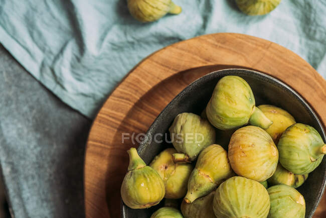 Figos verdes doces frescos e maduros, em uma tigela preta no prato de madeira servido na mesa de toalha azul, fruta orgânica sazonal. Também conhecido como figos brancos maduros — Fotografia de Stock