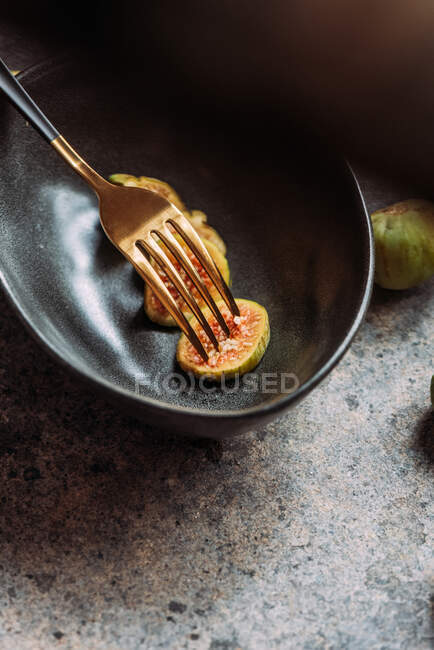 Trozos de higo verde en un moderno tazón negro sobre la mesa con textura grunge. concepto mínimo de comida. También conocido como higos blancos maduros - foto de stock