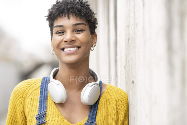 Dreamy smiling African American female in wireless headphones while standing on street looking at camera — Stock Photo