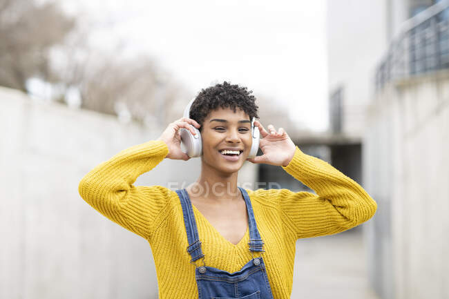 Dreamy smiling African American female in wireless headphones enjoying songs while standing on street — Stock Photo