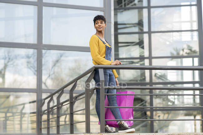 Délicieuse femme afro-américaine debout avec des sacs en papier en ville et regardant loin après des achats réussis — Photo de stock