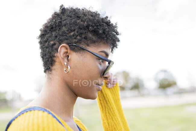 Vue latérale de la jeune femme afro-américaine dans des lunettes de soleil élégantes debout dans le parc et regardant loin — Photo de stock