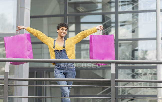 Délicieuse femme afro-américaine debout avec des sacs en papier en ville et regardant la caméra après des achats réussis — Photo de stock
