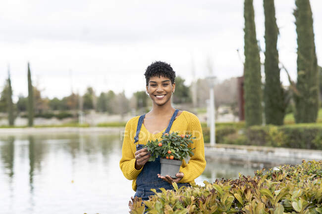 Joyful afro-americano feminino de pé com ramos com flores no parque na primavera e olhando para a câmera — Fotografia de Stock
