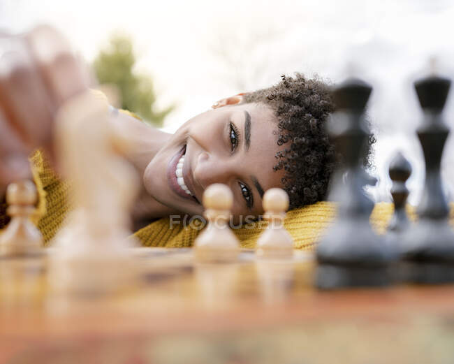 Von unten eine optimistische Afroamerikanerin, die im Park am Tisch sitzt und Schach spielt, während sie in die Kamera schaut — Stockfoto