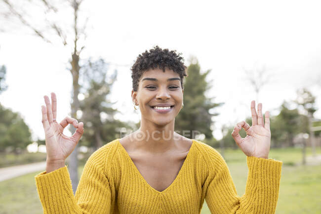 Mulher afro-americana encantada com mãos de mudra fazendo ioga no parque e olhando para a câmera — Fotografia de Stock