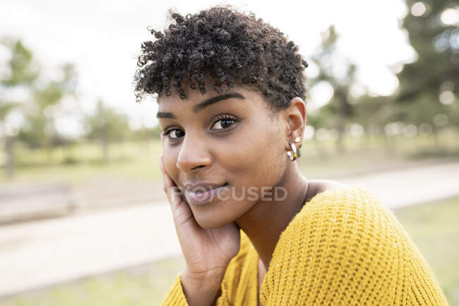 Glad African American femme avec une coiffure afro et dans une tenue à la mode penché sur la main et regardant la caméra dans le parc — Photo de stock