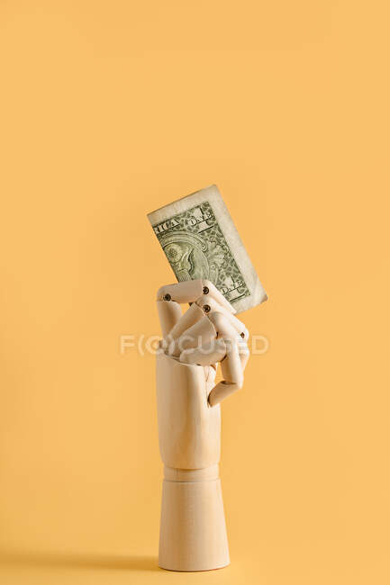 Dollarschein in hölzerner Hand auf orangefarbenem Hintergrund im Studio mit Finanzkonzept — Stockfoto