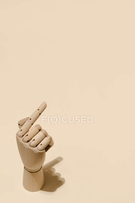 Alto ângulo de mão de madeira com o dedo indicador apontando para cima no fundo bege no estúdio — Fotografia de Stock
