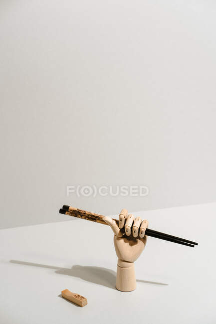 Creative wooden hand with ornamental bamboo chopsticks for Asian food on white background in studio — Stock Photo