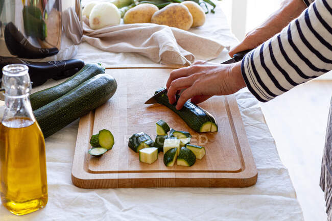 Vista laterale alto angolo di raccolto femminile in piedi a tavola e il taglio di zucchine fresche durante la preparazione di ingredienti per la minestra crema — Foto stock